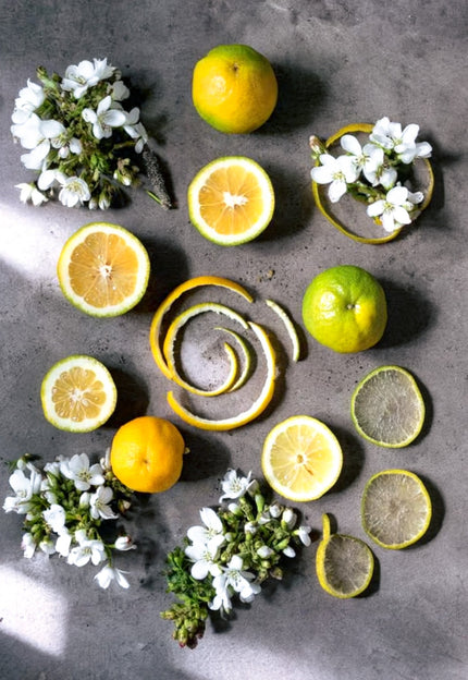 Fresh bergamot citrus and delicate neroli blossoms, core ingredients for the SE-LF Bergamot & Neroli collection, styled on polished concrete